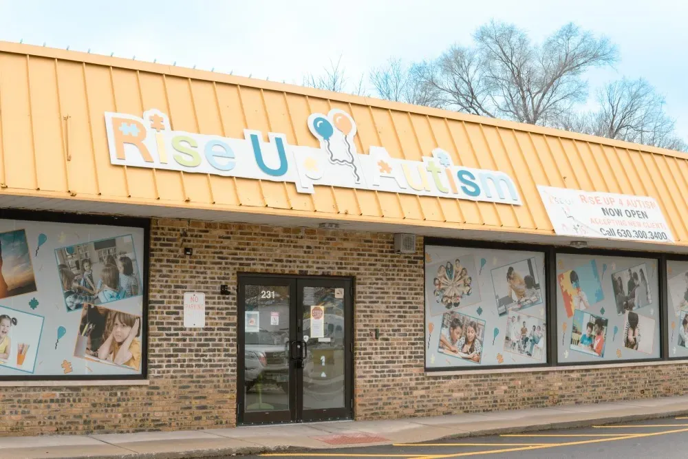 The Rise Up For Autism Aurora center storefront, with the branded sign and balloon logo mounted above the entrance and windows decorated with client photos.