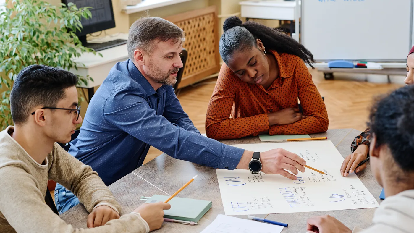Four colleagues around a table, one pointing at a hand-written plan they are working through together.
