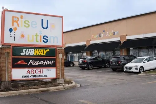 The Rise Up For Autism Joliet center in a strip mall, with the building sign reading Rise Up Autism alongside neighboring businesses.